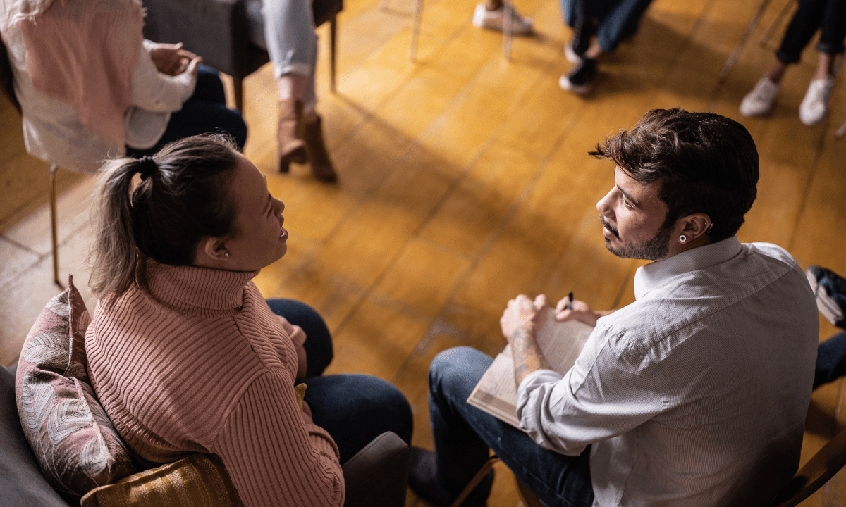Zia-Recovery-Center-Addiction-Center-Routines Support group therapy session with diverse adults standing in a circle, one person offering comfort with a hand on another’s shoulder, symbolizing connection and healing.